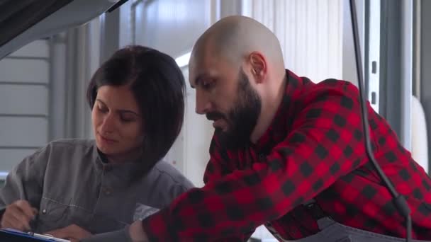 Dos mecánicos profesionales hembra y macho reparando un coche en el taller de reparación de automóviles. Servicio, reparación y mantenimiento de automóviles — Vídeo de stock