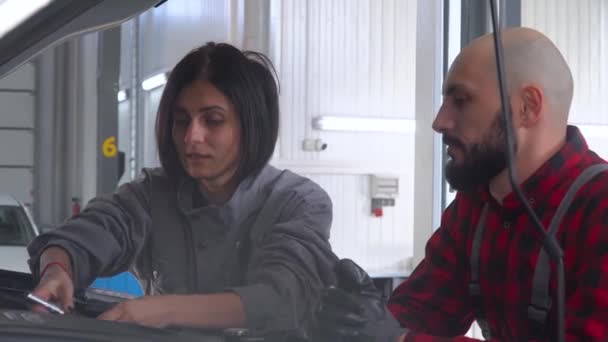 Dos mecánicos profesionales hembra y macho reparando un coche en el taller de reparación de automóviles. Servicio, reparación y mantenimiento de automóviles — Vídeos de Stock