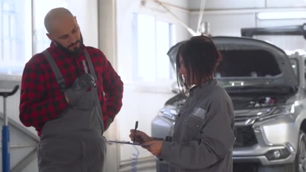 Dos mecánicos profesionales femenino y masculino en taller de reparación de automóviles. Servicio, reparación y mantenimiento de automóviles — Vídeos de Stock