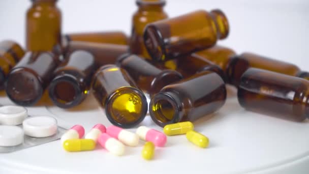 Медичні пляшки та різнокольорові таблетки на білому тлі. Виготовлення таблеток, таблеток та інших ліків. Фармацевтична промисловість — стокове відео