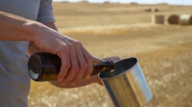 Bir adam buğday tarlasında balyalı metal bir bardağa bira döker. Taze bira, güneş enerjisi