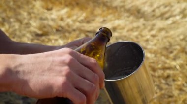 Bir adam buğday tarlasında balyalı metal bir bardağa bira döker. Taze bira, güneş enerjisi