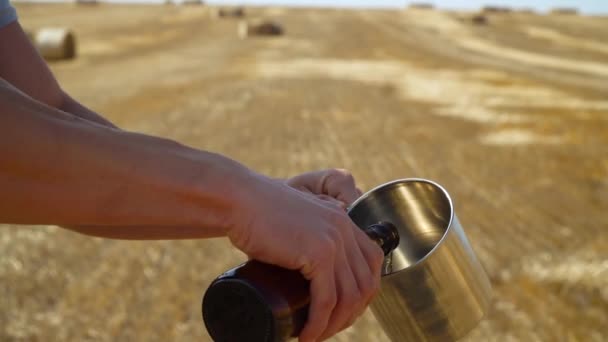 Um homem derrama cerveja num copo de metal num campo de trigo com fardos. Cerveja fresca, campo solar — Vídeo de Stock