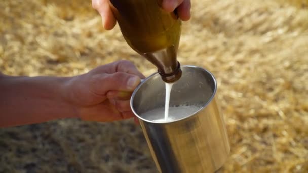 Een man giet bier in een metalen glas op een tarweveld met balen. Vers bier, zonneveld — Stockvideo