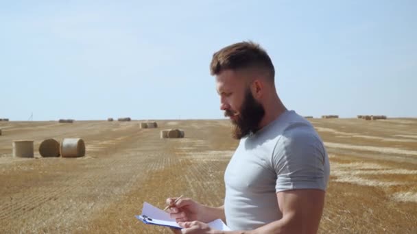 Vousatý farmář drží tabletu s písmenem v ruce na pozadí balíků sena — Stock video