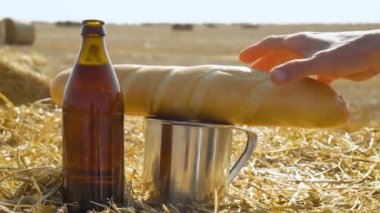 Buğday tarlasında balyalarla bira, ekmek ve metal camlar. Adam ekmeği alır