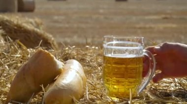 Buğday tarlasında balyalarla bira, ekmek ve metal camlar. Adam birayla bardağı alır.