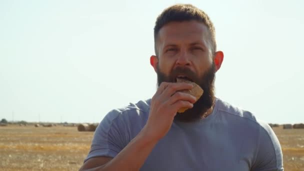 Man eating bread on a wheat field with bales. Bread harvest — Stock Video