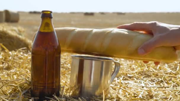 Beer, bread and metal glass on a wheat field with bales. Man puts the bread — Stock Video