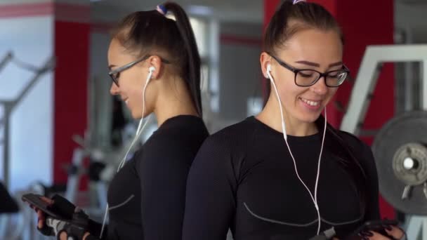 年轻姑娘带着耳机在体育馆里用智能手机。 女孩听音乐 — 图库视频影像