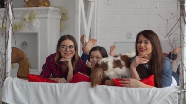 Две счастливые женщины и маленькая девочка с собакой лежат на кровати — стоковое видео