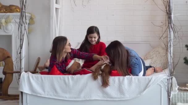 Zwei glückliche Frauen und ein kleines Mädchen mit Hund liegen auf dem Bett — Stockvideo