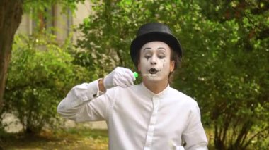 Eğlenceli pandomimci dışarıda sabun köpüğü üflüyor.