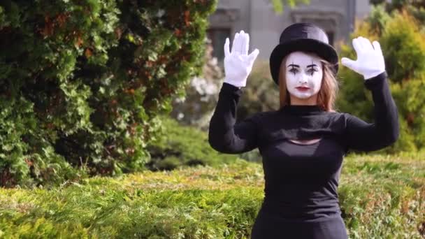 Jeune drôle de mime femelle derrière une boîte ou un mur de verre invisible. Mime sur le parc montre pantomime — Video