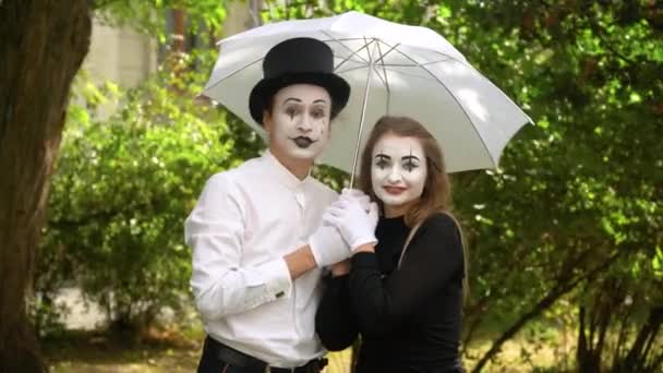 Dwóch aktorów mimuje z parasolem na parku patrząc w kamerę i uśmiechając się na zielonym tle w parku. Kochająca się para w parku — Wideo stockowe