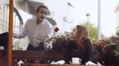Two happy mime on a date in the cafe. Happy man giving a flower to his girlfriend