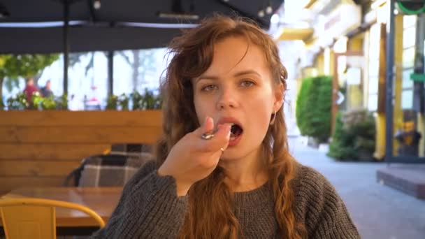 Jonge vrouw eet een chocolade taart in een straat cafe, close-up — Stockvideo