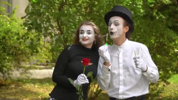 Una pareja feliz en una cita. Divertido mimo soplando burbujas de jabón al aire libre. Chica con flor — Vídeos de Stock