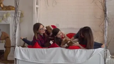 İki mutlu kadın ve köpekli küçük kız yatakta yatıyor.