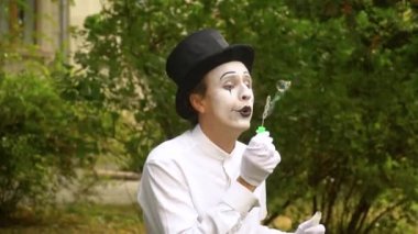 Eğlenceli pandomimci sabun köpüklerini yavaş çekimde dışarı üflüyor.