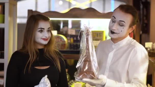 Happy man mimespeler geeft een chocolade eiffeltoren aan zijn vriendin. Twee gelukkige mimespelers op een date in het café — Stockvideo