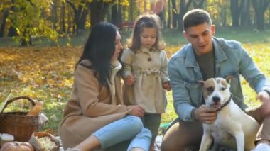Anne ve baba, kızları ve köpekleri dışarıda eğleniyor. Sonbahar parkında piknik