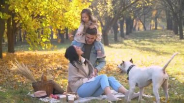 Sonbahar parkında köpekli mutlu bir aile. Babasının sırtında küçük bir kız. Düş