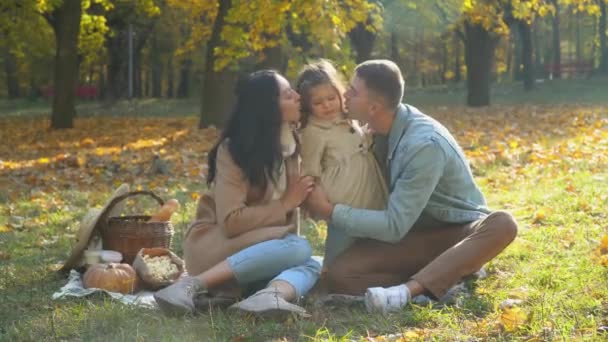 Madre y padre con hija divirtiéndose al aire libre. Picnic en el parque de otoño — Vídeo de stock
