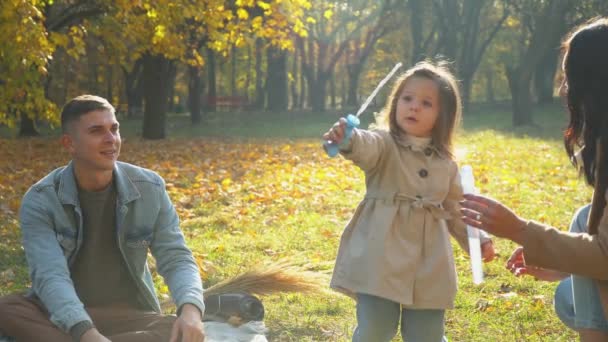 Madre y padre con hija y perro divirtiéndose al aire libre. Picnic en el parque de otoño — Vídeo de stock