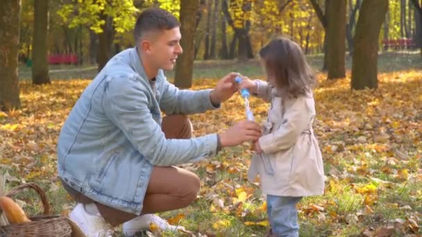 Apa légbuborékokat fúj a kislányával az őszi parkban. — Stock videók