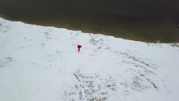 Cansado Papai Noel vai com um saco de presentes ao longo da costa ártica nevada do oceano. Vista superior — Vídeo de Stock