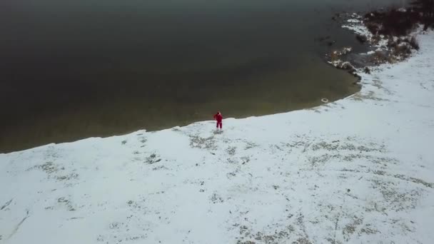 サンタクロースは湖の雪の海岸にギフトバッグで立っています。北極圏のサンタ。トップ表示 — ストック動画