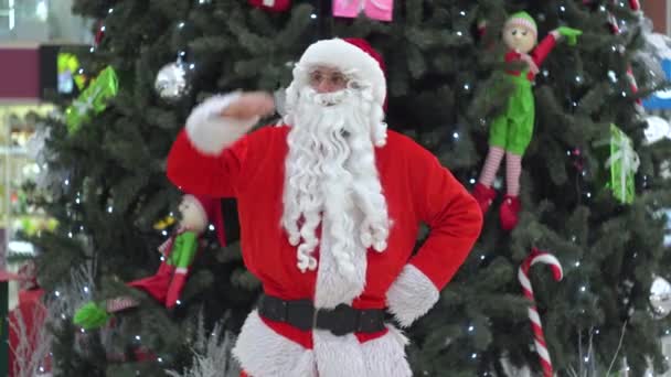Санта Клаус стоит на торговом центре возле рождественской елки — стоковое видео