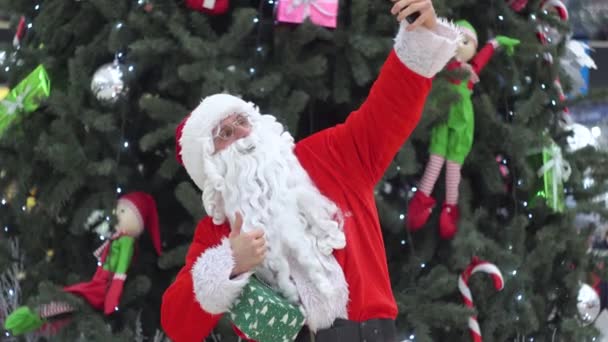 Santa Claus hace selfie en el centro comercial cerca del árbol de Navidad — Vídeos de Stock