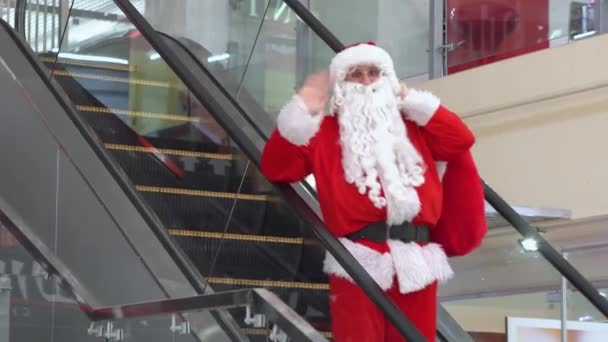 Tiro de Papai Noel com saco em movimento na escada rolante, sobe a escada rolante em um grande centro de negócios — Vídeo de Stock