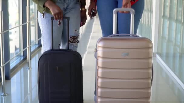 Dos niñas afroamericanas viajan llevando su equipaje y moviéndose sobre el salón de la terminal, vista trasera. La gente se está preparando para embarcar y salir — Vídeos de Stock