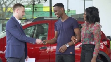 Beyaz tenli yakışıklı araba satıcısı Afrikalı Amerikalı müşterilerine yeni bir arabanın anahtarlarını veriyor.
