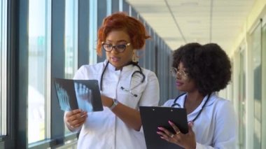 İki Afrika kökenli Amerikalı doktor, bacağının röntgenini çekiyorlar ve içeride tutuyorlar. İki uzman kollarında bacağın şeffaf görüntüsünü tutuyor ve dikkatlice araştırıyor.