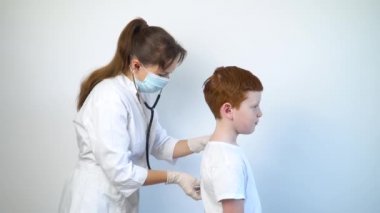 Stetoskop kullanan kadın bir doktor, hastaneye yaptığı tıbbi ziyarette hasta bir çocuğun akciğerlerini ve kalbini dinliyor.