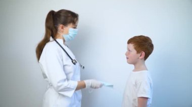 Kadın doktor bir çocuğa koruyucu maske veriyor.