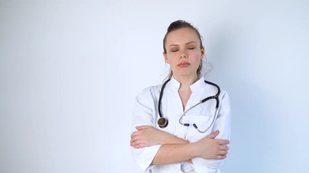 Retrato de una joven doctora con una bata blanca y un estetoscopio sobre fondo blanco en un hospital — Vídeos de Stock