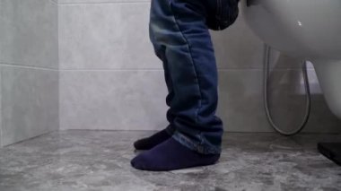 Kot pantolonlu küçük çocuk tuvalette oturuyor. Çocuk pantolonunu çıkarıyor.