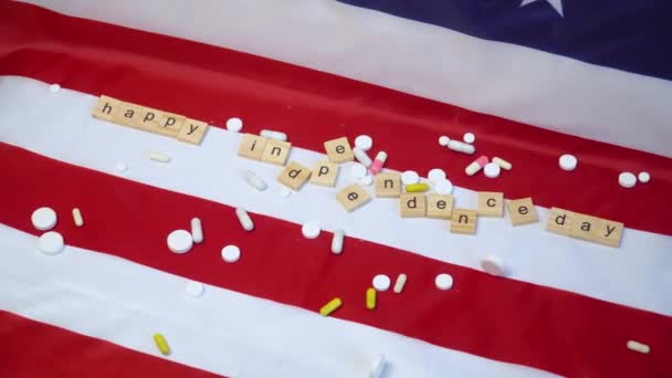 Смешанные таблетки на флаге США с надписью С Днем Независимости. Коронавирус в США. Победа над коронавирусом. Вакцина Ковида-19 — стоковое видео