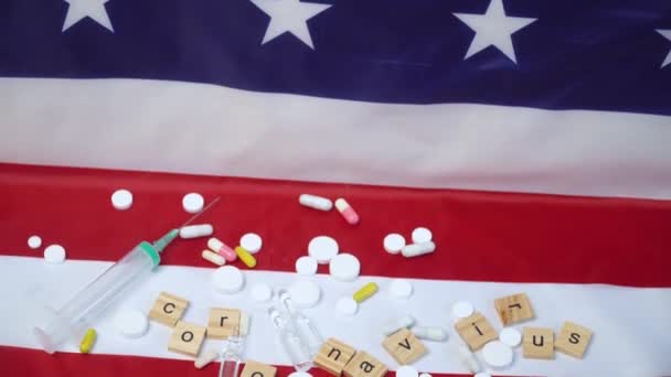 Смешанные таблетки и шприц на флаге США с надписью коронавирус. Коронавирус в США. Победа над коронавирусом. Вакцина Ковида-19 — стоковое видео