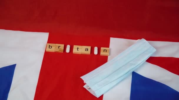 Змішані таблетки з блакитною захисною маскою на прапорі Великої Британії з написом "Британія". Міністерство охорони здоров'я Великої Британії. Коїд-19. — стокове відео