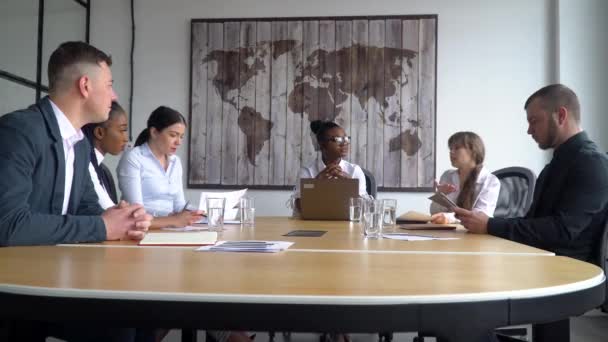 Различные сотрудники собрались вместе на брифинге сесть за стол, африканский американский сотрудник принимает участие в групповой дискуссии вырабатывают идеи и пути решения проблем, предлагая возможности — стоковое видео