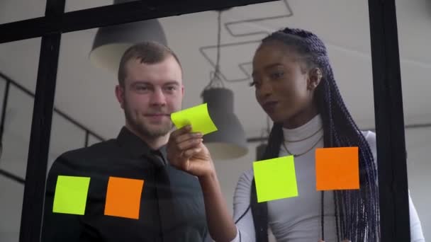 Företag företag multietniska människor med hjälp av klibbiga anteckningar, lösa strategi på glas whiteboard. Gruppledare kvinna visar lösning för projektets deadline i kontorsmöte — Stockvideo