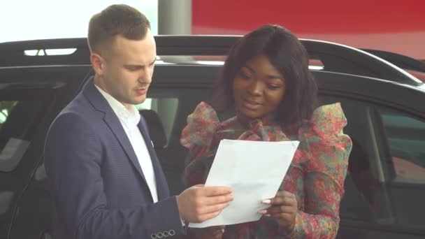 Professionnel vendeur de voitures raconte acheteur afro-américain intéressé sur la voiture de luxe dans le salon de l'automobile. Entreprise automobile, vente de voitures, concept de technologie et de personnes — Video