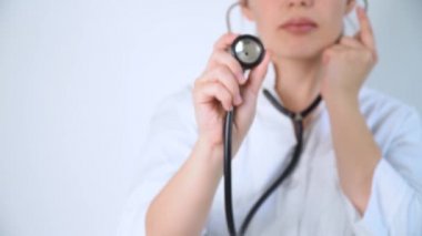 Hastanenin beyaz arka planında steteskopu olan beyaz önlüklü genç bir doktorun portresi.