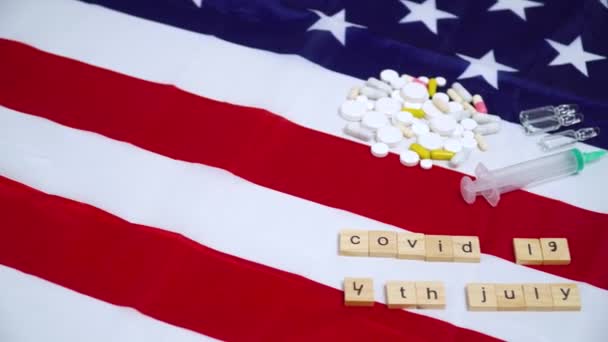 Wort Coronavirus und 4. Juli aus Buchstaben auf der Flagge der USA. Covid - 19 Virus-Konzept. Pillen und Spritze auf US-Flagge — Stockvideo